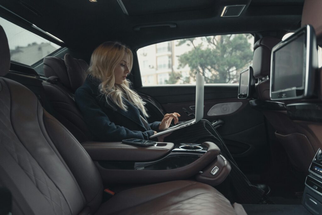 A businesswoman working on a laptop inside a luxury car, showcasing professionalism and modern technology.